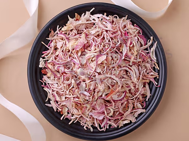 Bowl of red onion flakes on a beige surface