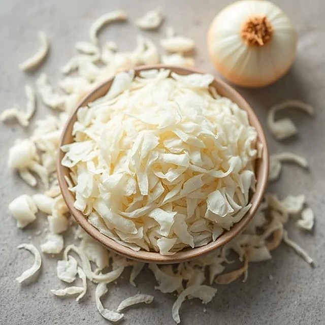 Bowl of white onion flakes beside a whole onion